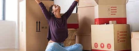 Woman raising arms celebrating new home while sitting amongst moving boxes