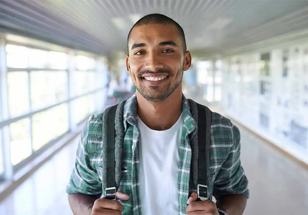 Student smiling in hallway holding backpack straps