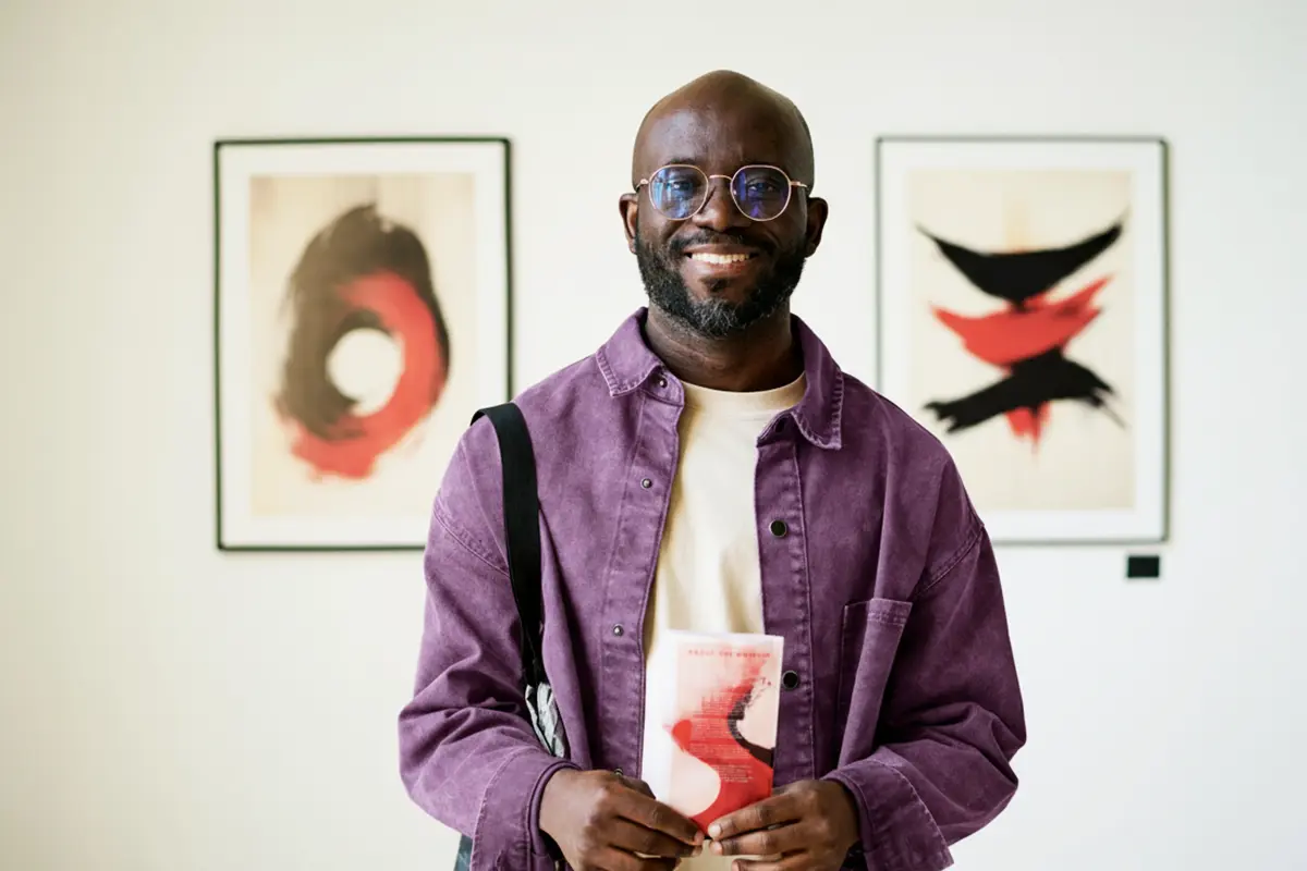 Smiling man with earphones using a smartphone by a window.