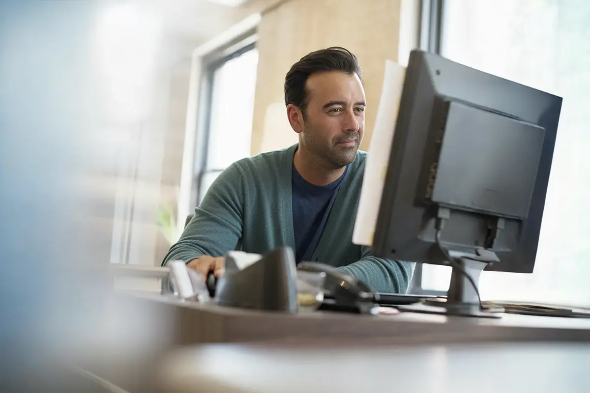Smiling man with earphones using a smartphone by a window.