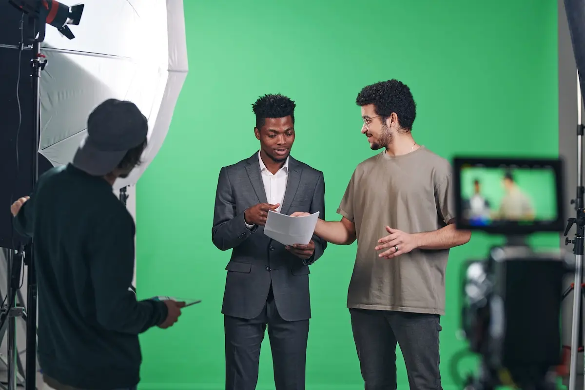 A group of three men, including an actor in a suit, on a film set with a green screen, representing creative professionals who must navigate unpredictable paychecks and plan for income peaks and valleys.