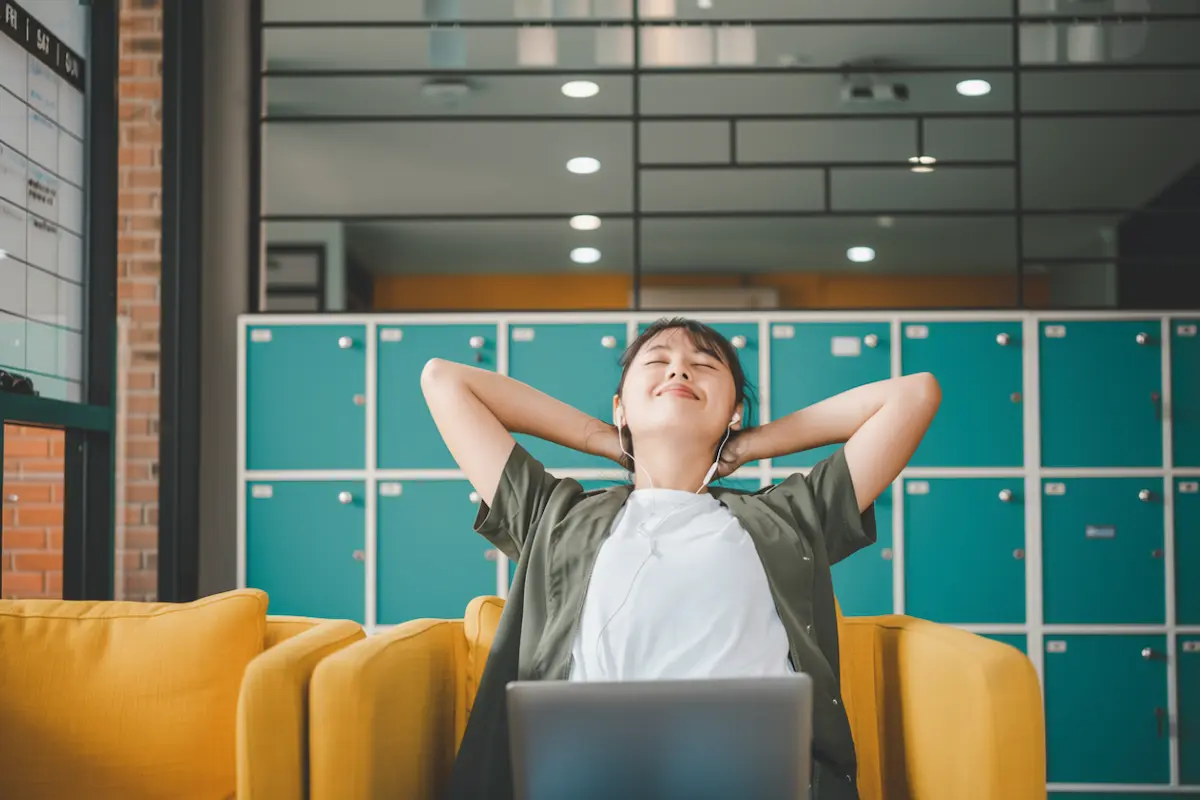 A young woman, a freelancer, relaxes with her hands behind her head and headphones on in front of a laptop, symbolizing the peace of mind that comes from successfully managing irregular income.