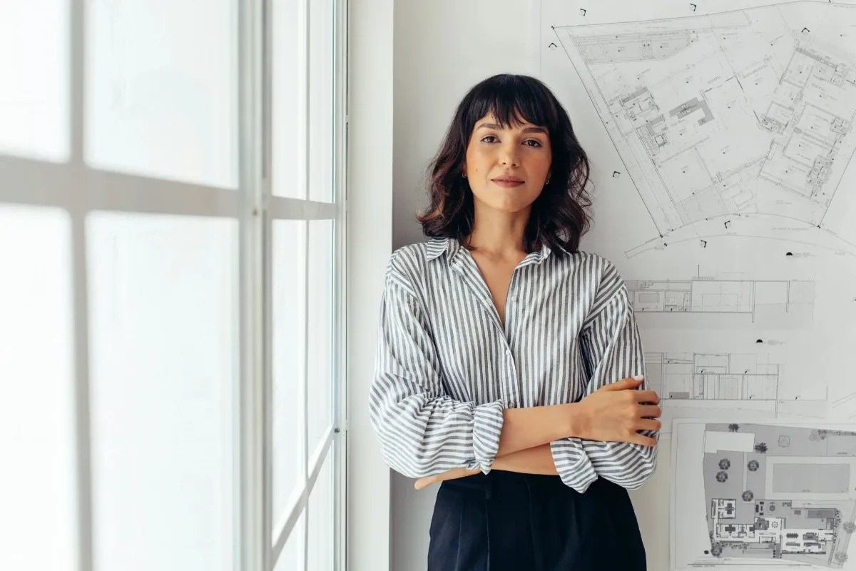 Creative professional standing beside architectural plans, illustrating borrowing for freelancers seeking business financing through Creative Arts Financial. 