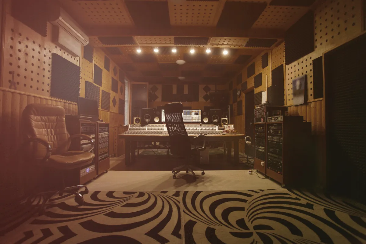 Recording studio with mixing console, audio equipment, speakers, and soundproof panels under warm lighting.