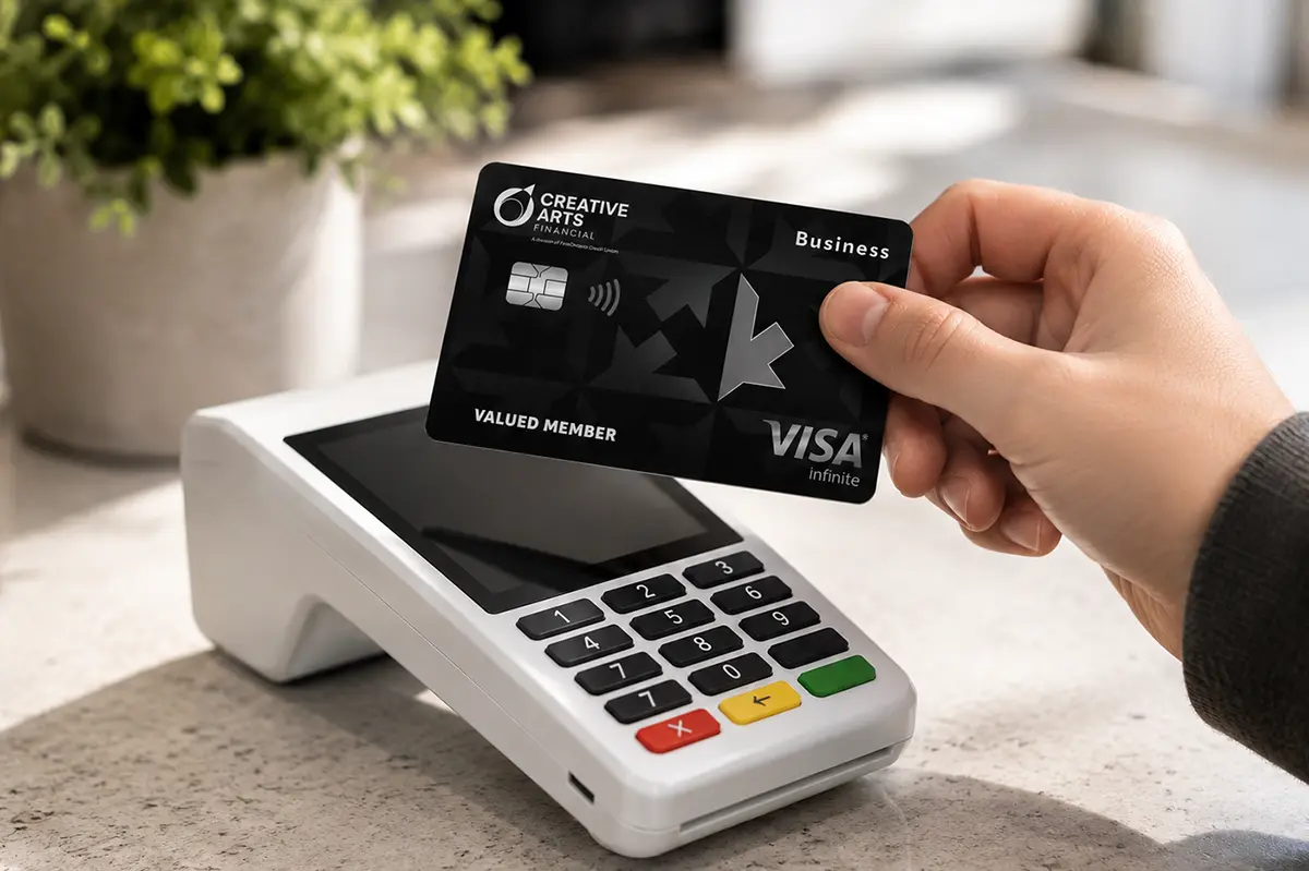 Making a secure contactless payment with a Creative Arts Financial Visa Business card. Hand holding a Creative Arts Financial Visa Infinite Business credit card near a teal card reader for a contactless payment.