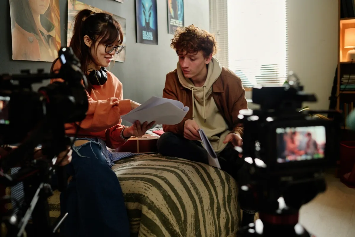 Two filmmakers reviewing a script together on a film set with cameras positioned nearby.