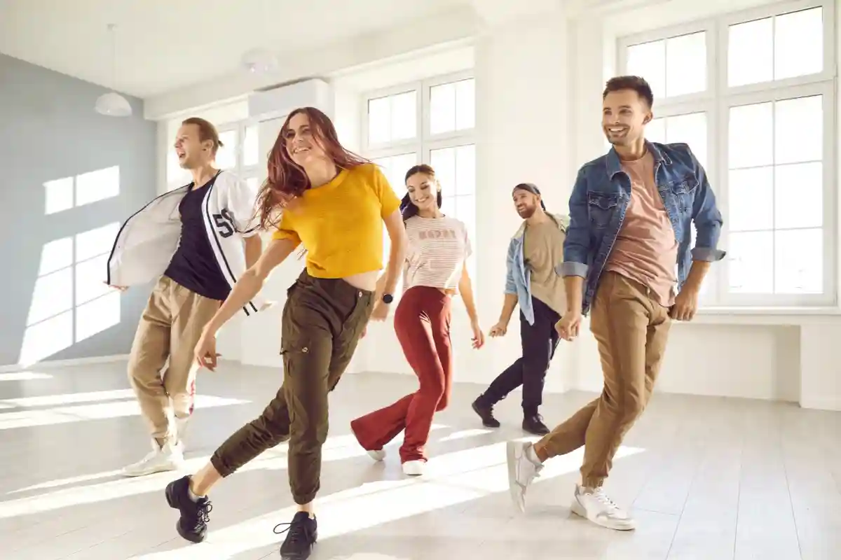 Group of dancers performing a choreographed routine in a bright studio with large windows.